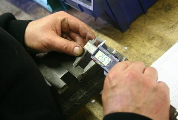 Quality inspector measuring a metal part with a digital caliper